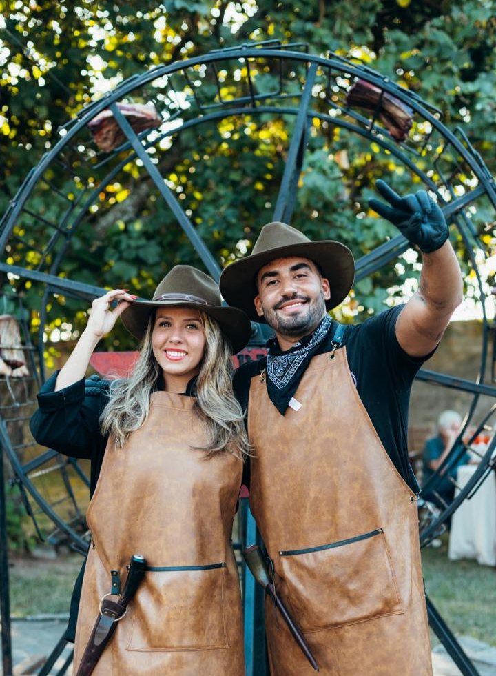 Equipe do Brasaria BBQ de avental de couro e chapéu em frente à roda gigante de costela