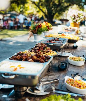 Mesa de buffet montada ao ar livre com rechauds e saladas